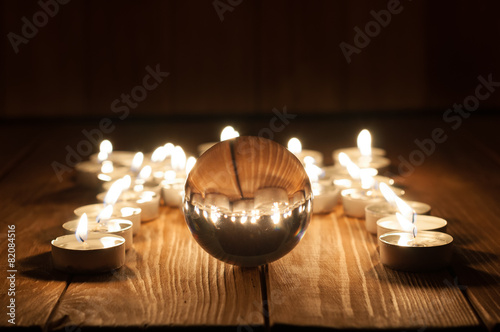 Fotografie, Obraz Glass transparent ball and burning candles on old wooden
