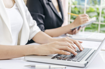 two business workers typing in laptop and taking note