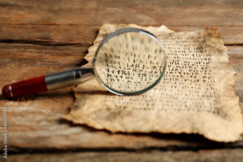 Grunge paper with hieroglyphics with magnifier on wooden background