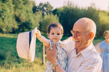 Baby girl playing with hat of senior man outdoors