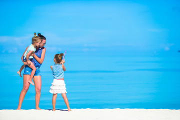 Adorable little girls and young mother on tropical white beach