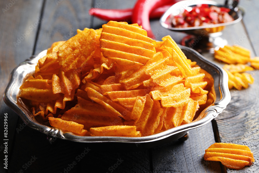 Delicious potato chips on plate on wooden table close-up