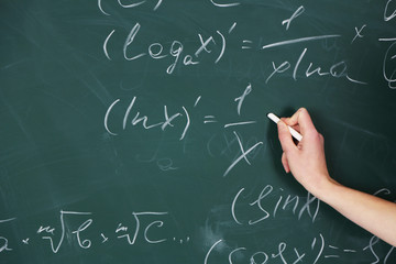 Female hand writing formulas on blackboard with chalk, close up