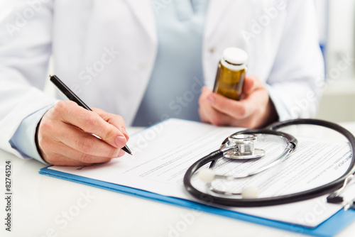 Fotografía Médico femenina rellenar el formulario médico sosteniendo la botella de la medic