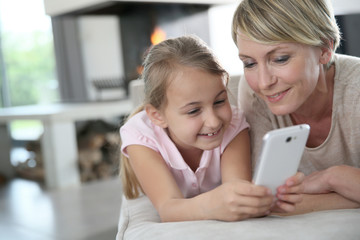 Wall Mural - Mother and young girl playing with smartphone at home