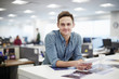 © Mint Images - A man smiling and leaning forward on his desk.