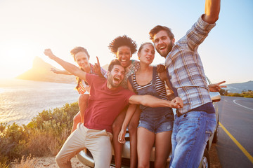group of friends standing by car on coastal road at sunset