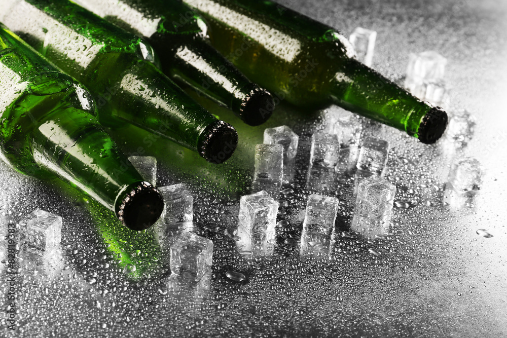 Glass bottles of beer with ice cubes on wet table background