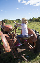 Little Girl Playing In A Field On An Old Rusting Farm Tractor