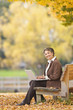 © Don Mason/Blend Images - African woman using laptop on park bench in autumn
