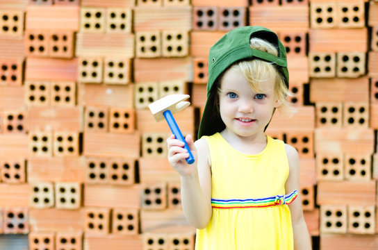 Cute kid playing with construction tools on orange bricks backgr