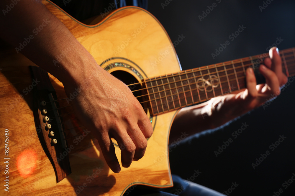 Young man playing on acoustic guitar on dark background