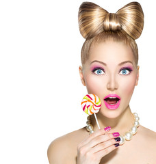 Funny girl with bow hairstyle eating colorful lollipop