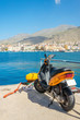 Orange scooter standing on wharf of Greek harbour with city budi