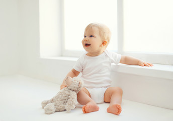 cute smiling baby with teddy bear toy sitting at home in white r