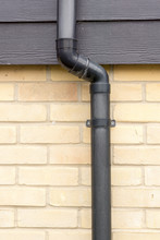 Close Up Of A Black Drainage Pipe And Clip On A Brick Wall