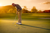 Fototapeta Desenie - Male golf player putting at sunset.