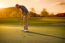 Male Golf Player Putting At Sunset.