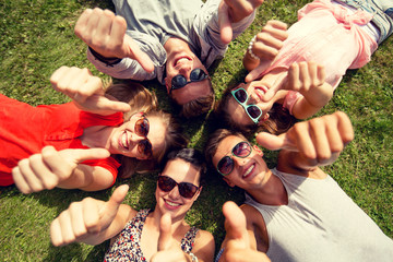 Wall Mural - smiling friends showing thumbs up lying on grass