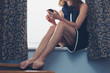 © LoloStock - Woman sitting on window sill using smartphone