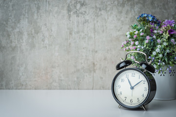 Old-time alarm clock on a white table with flowers