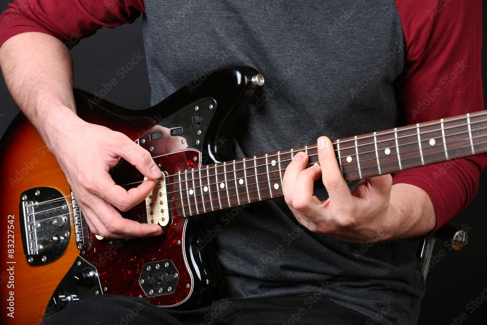 Young man playing on electric guitar close up