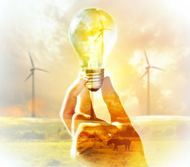 Double exposure. Hand holding light bulb on a wind turbine backg