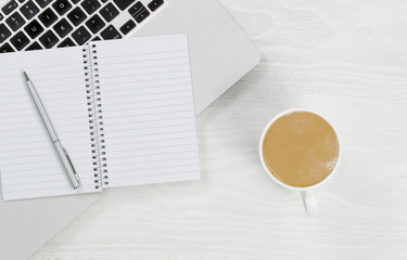 Laptop computer with coffee and blank notepad on white desktop