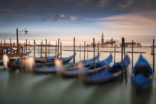 Italy, Venice, Moored Gondolas In Row With City Skyline In Distance