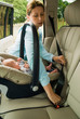 © RooM The Agency - Mother strapping baby son in back seat of a car