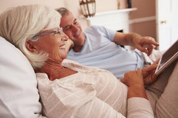 Wall Mural - Senior Couple Lying In Bed Looking At Digital Tablet