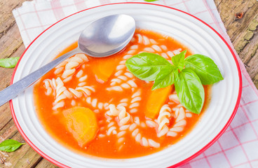 Tomato soup with pasta and fresh basil in white bowl