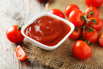 Fresh tomatoes with bowl of ketchup on wooden background