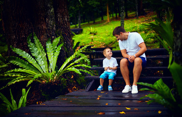 Wall Mural - happy father and son sitting on wooden stairs in rain forest