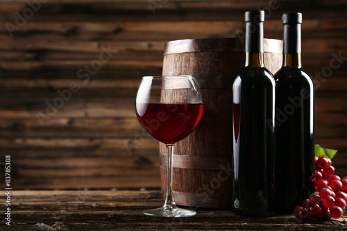 czerwone-wino-w-kieliszku-wraz-z-butelkami-na-brazowym-drewnianym-tle