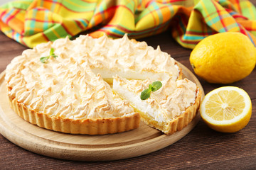 Lemon meringue pie on cutting board on wooden background