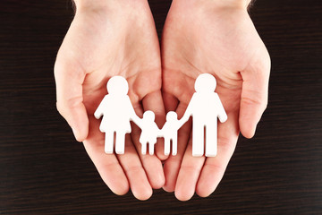 Wall Mural - Female hands with paper family on wooden background