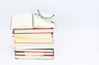 Open notebook on the stack of colorful books, glasses on the top