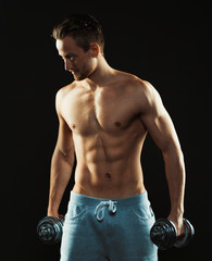 Athletic attractive man with dumbbells on the black