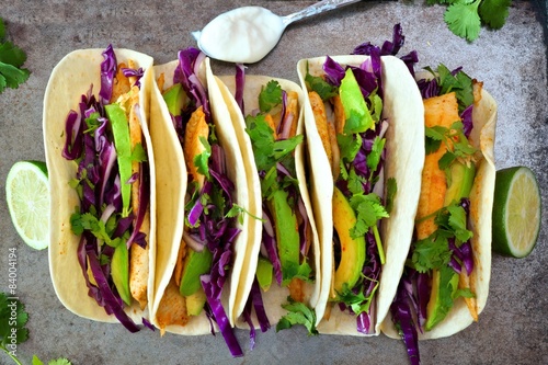 Vászonkép Fish tacos with red cabbage, avocado and lime on rustic tray