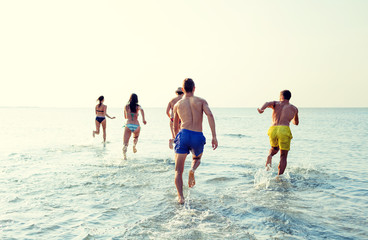 Wall Mural - smiling friends running on beach from back