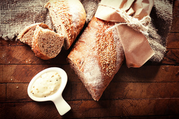 Poster - Fresh baked bread wrapped in paper and bowl with sauce, on wooden background