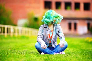 Beautiful alternative young woman with green hair sits on grass