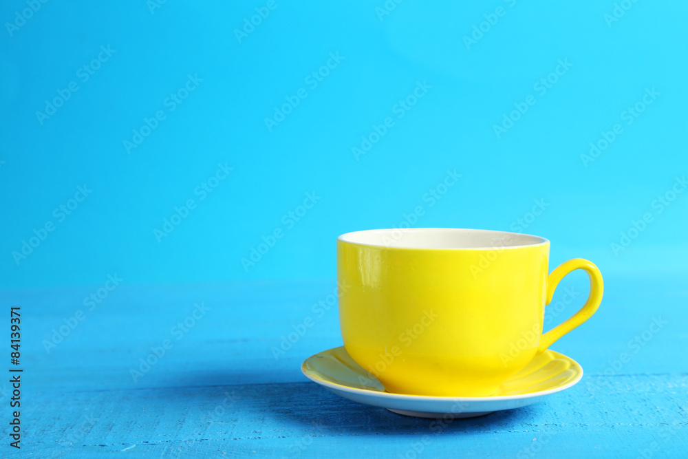 Yellow cup on blue wooden background - obrazy, fototapety, plakaty 
