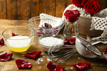 Making candied rose flower petals with egg whites and sugar, on wooden background