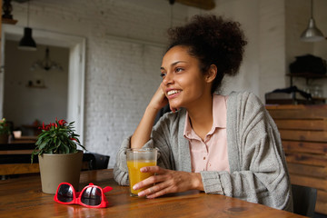 Wall Mural - Smiling young woman sitting at home with glass of orange juice