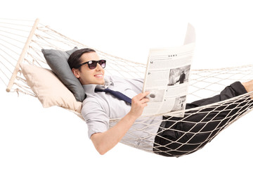 Wall Mural - Relaxed young man reading a newspaper and lying in a hammock