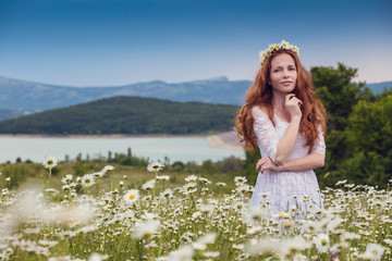 Wall Mural - Beautiful young girl with curly red hair in camomile field