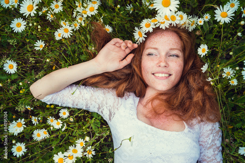 Fotografía Hermosa joven con cabello rojo rizado en el campo de manzanilla