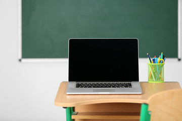 Canvas Print - Wooden desk with stationery and laptop in class on blackboard background